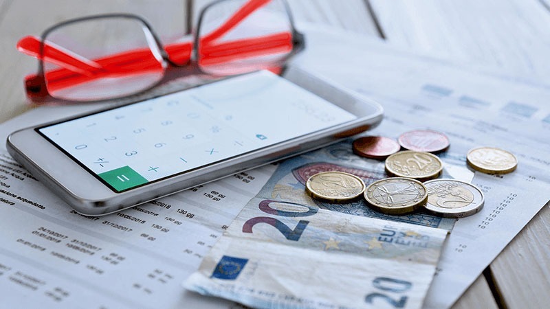 Glasses, phone with calculator app, coins, and Euro banknotes on a financial document.
