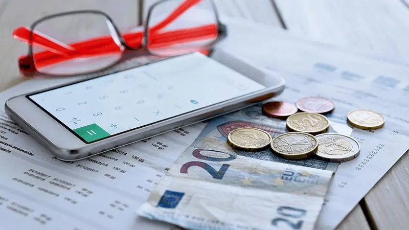 Glasses, phone with calculator app, coins, and Euro banknotes on a financial document.