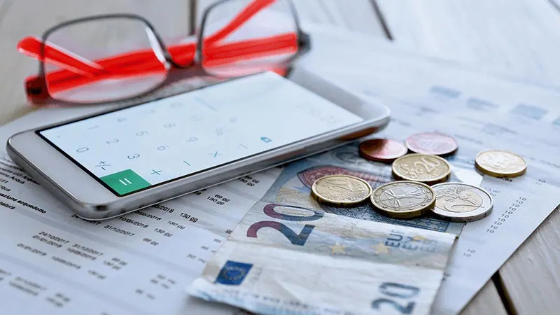 Un téléphone, des lunettes, des pièces et des billets de 20 euros sont posés sur un document imprimé.