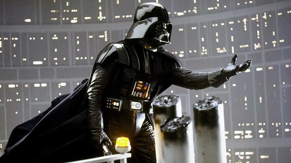 Un personnage en costume noir avec un casque se tient devant une fenêtre avec des lumières.