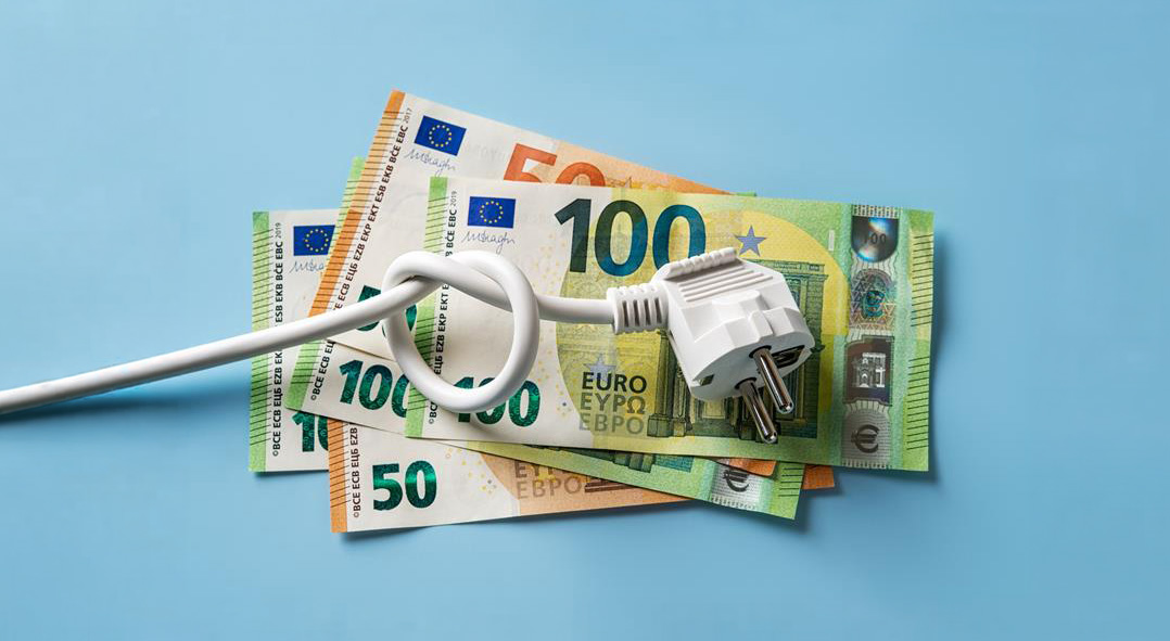 Een stekker met geknoopt snoer ligt op eurobiljetten, als beeld voor energiekosten of stijgende elektriciteitsprijzen.