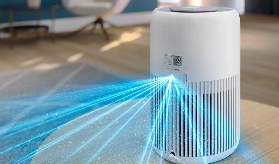 White cylindrical air purifier on a table projects bright blue beams that reveal floating dust across the spacious, sunlit living room.