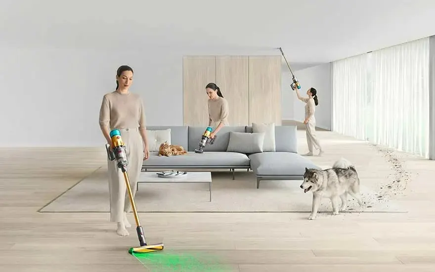 Trois aspirateurs nettoient un salon moderne avec un canapé gris, un chat, un chien et des planchers en bois.