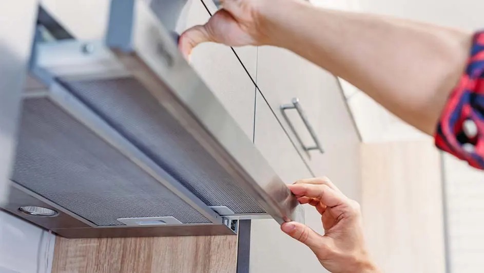 Une hotte de cuisine en acier inoxydable est tirée vers le bas sous une armoire de cuisine blanche.