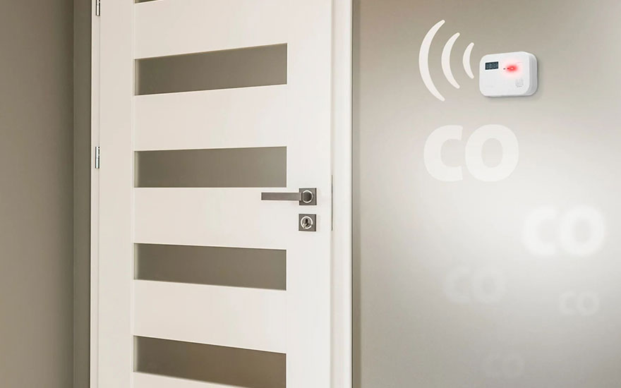 Une porte blanche avec des fenêtres rectangulaires est à côté d'un détecteur de monoxyde de carbone sur un mur gris.