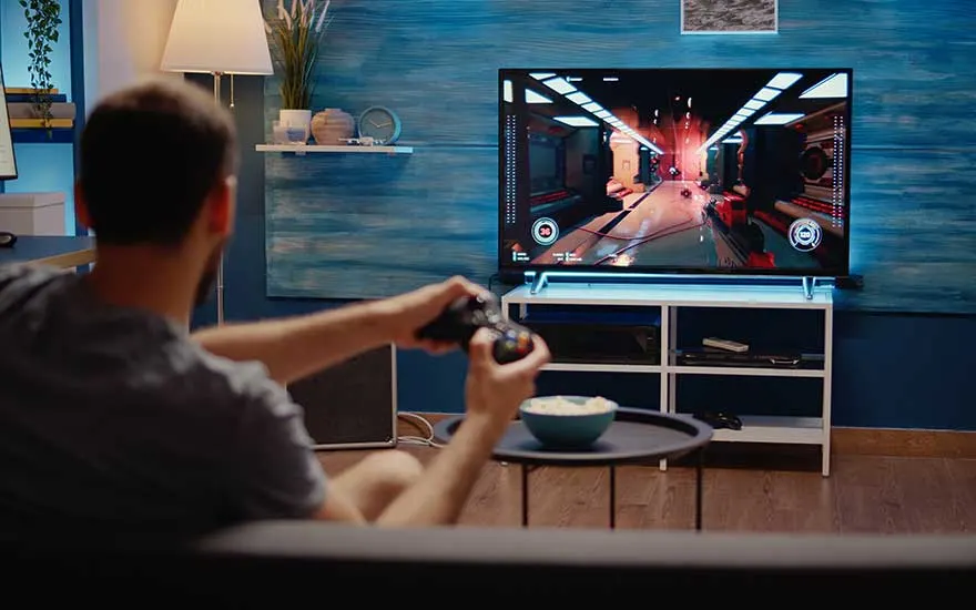 Un homme joue à un jeu vidéo sur une télévision. Une collation est sur une table. Le mur est bleu.