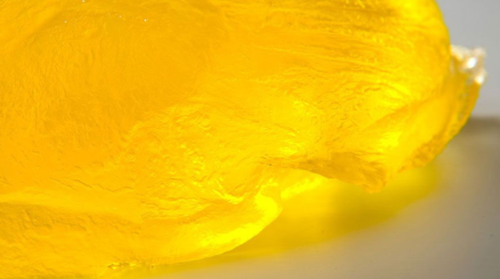 Een close-up van een gele, doorschijnende geleiachtige substantie op een glad, lichtgekleurd oppervlak.
