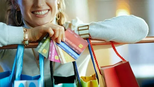 Diverse creditcards en boodschappentassen hangen aan een koperen stang. De tassen zijn blauw, rood en geel.