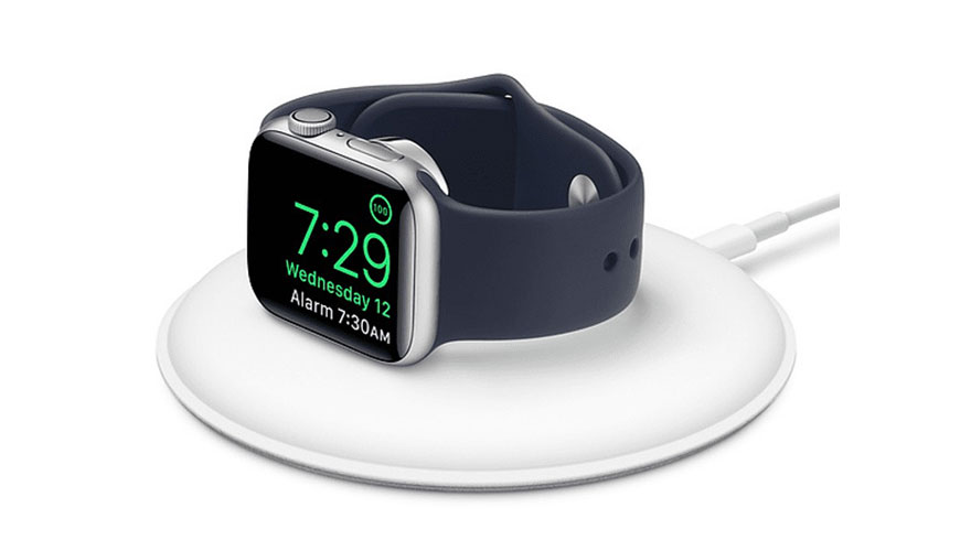 Une montre intelligente argentée avec un bracelet bleu foncé sur un chargeur blanc rond. L'écran affiche 7:29.
