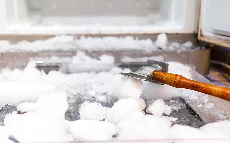 Un réfrigérateur blanc est rempli de glace. Un outil à manche en bois est utilisé pour casser la glace.