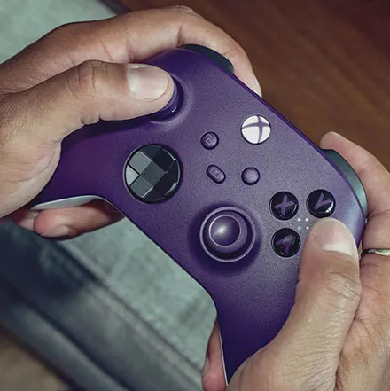 Persoon houdt paarse Xbox controller vast, moderne gamepad met joysticks en knoppen, gaming setup op houten tafel, casual gaming.