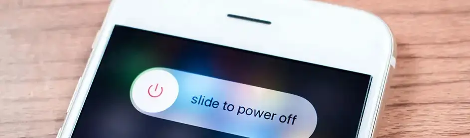 Image d'un smartphone blanc sur une table en bois, affichant un curseur "slide to power off".