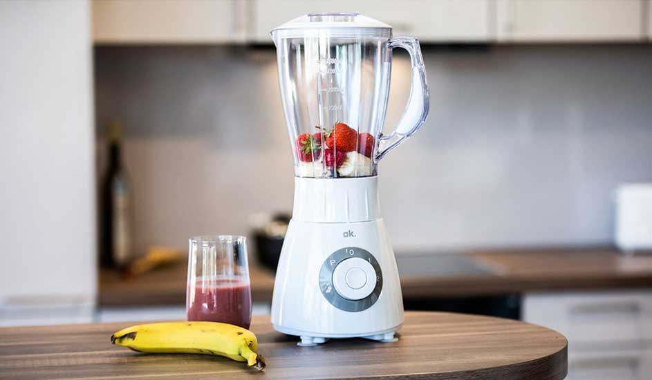 Witte blender met aardbeien en banaan, glas smoothie en banaan op een houten tafel in de keuken.