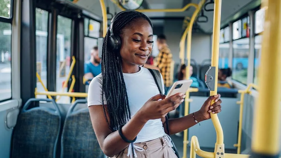 Intérieur d'un bus avec des sièges bleus et des barres jaunes. Une personne tient un téléphone.