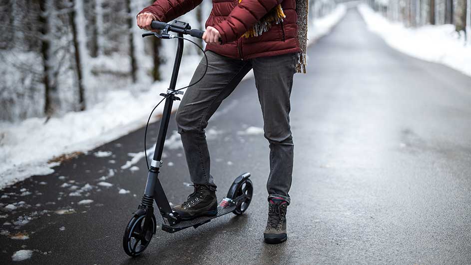 Een zwarte step staat op een weg in een winterlandschap met bomen en sneeuw.