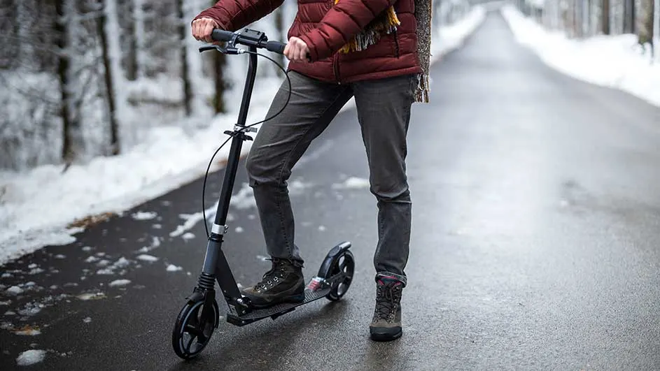 Een zwarte step staat op een weg in een winterlandschap met bomen en sneeuw.