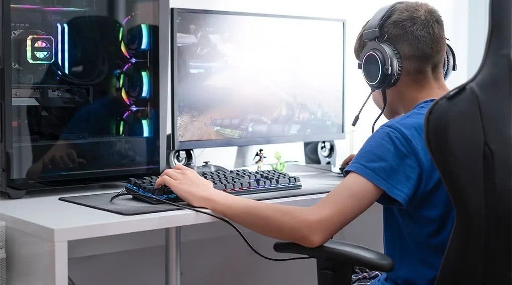 Un ordinateur avec un écran, un clavier et une souris sur un bureau blanc, avec une tour d'ordinateur éclairée à gauche.