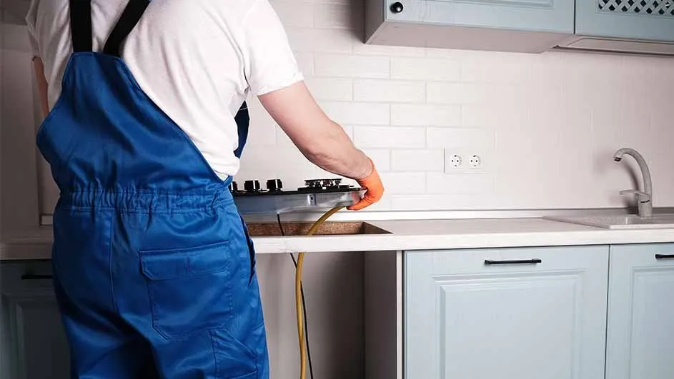 A kitchen scene shows blue cabinets, a white countertop, and a cooktop being installed. A yellow wire hangs below the counter.