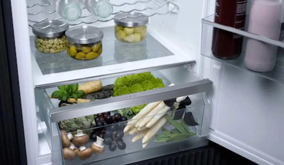 Een open koelkast gevuld met glazen potten, groenten en flessen op witte planken. Onderin liggen champignons, asperges en druiven.