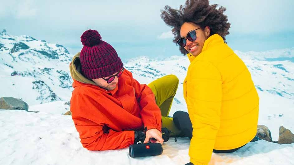 Deux personnes assises dans la neige avec un haut-parleur noir. L'arrière-plan montre une montagne enneigée.