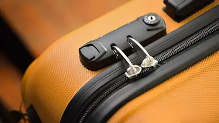 Gros plan d'une valise orange avec une fermeture éclair noire et un cadenas TSA noir et argenté.