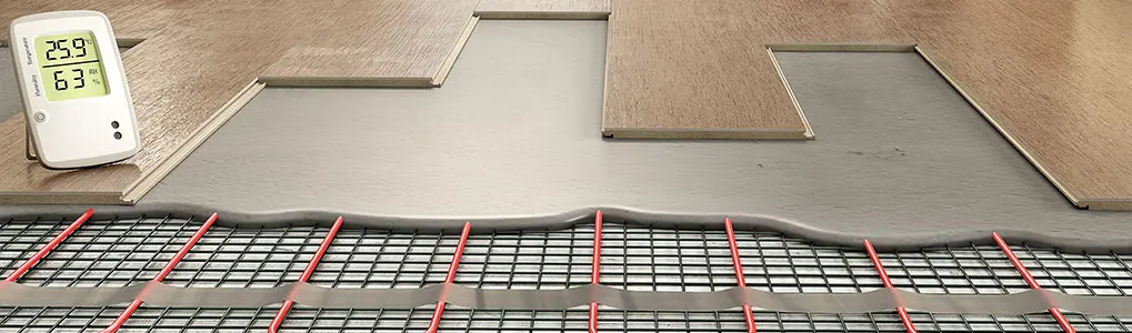 Vloerverwarming installatie met houten vloerdelen. Een witte thermostaat toont 25.9 en 63 graden.
