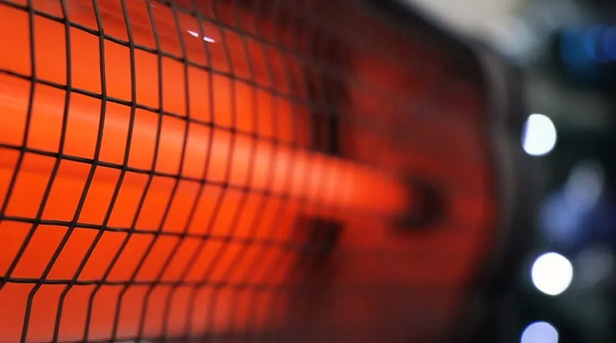 Gros plan sur un chauffage rougeoyant protégé par une grille noire, avec des lumières floues à l'arrière-plan.