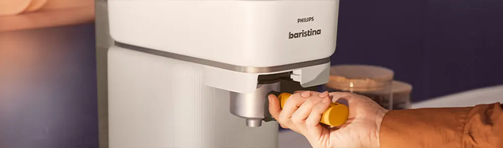 Een witte Philips Baristina koffiemachine met een hand die een gele filter vasthoudt.