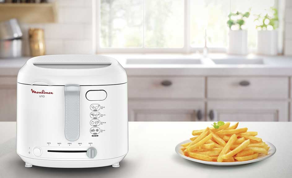 Une friteuse blanche est sur un comptoir de cuisine blanc avec une assiette de frites dorées.