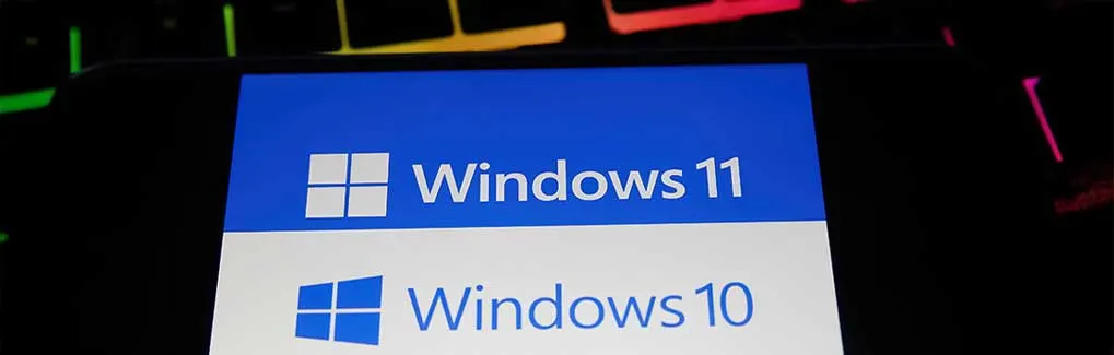 Un écran de téléphone affiche les logos de Windows 11 (bleu) et Windows 10 (blanc), sur un clavier noir éclairé.