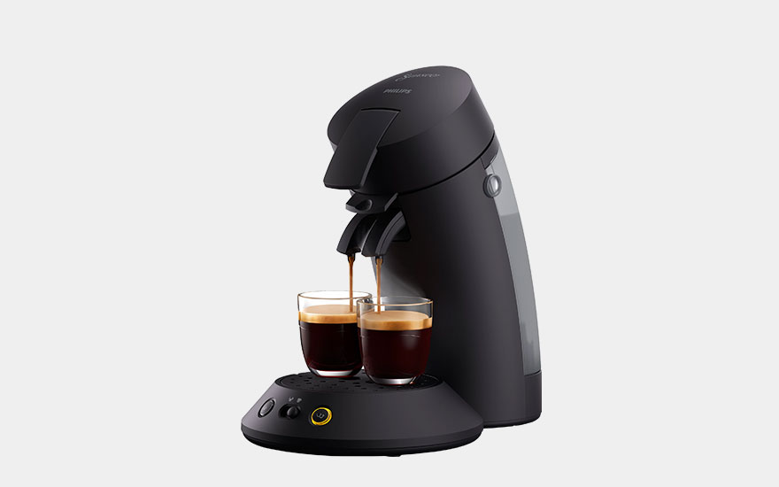 White coffee maker with a black base and a glass of layered latte on a grey background.