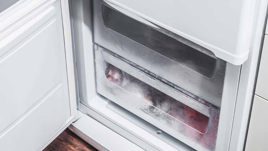 Un réfrigérateur blanc ouvert montre des tiroirs de congélation en plastique transparent, dont un avec des aliments congelés.