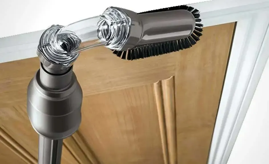 Un aspirateur avec brosse nettoie le dessus d'une porte marron dans un cadre de porte blanc. La brosse est grise et noire.