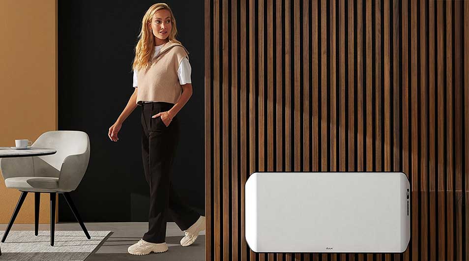 A room features a white heater against a wood-slat wall, with a table, chair, and rug visible.