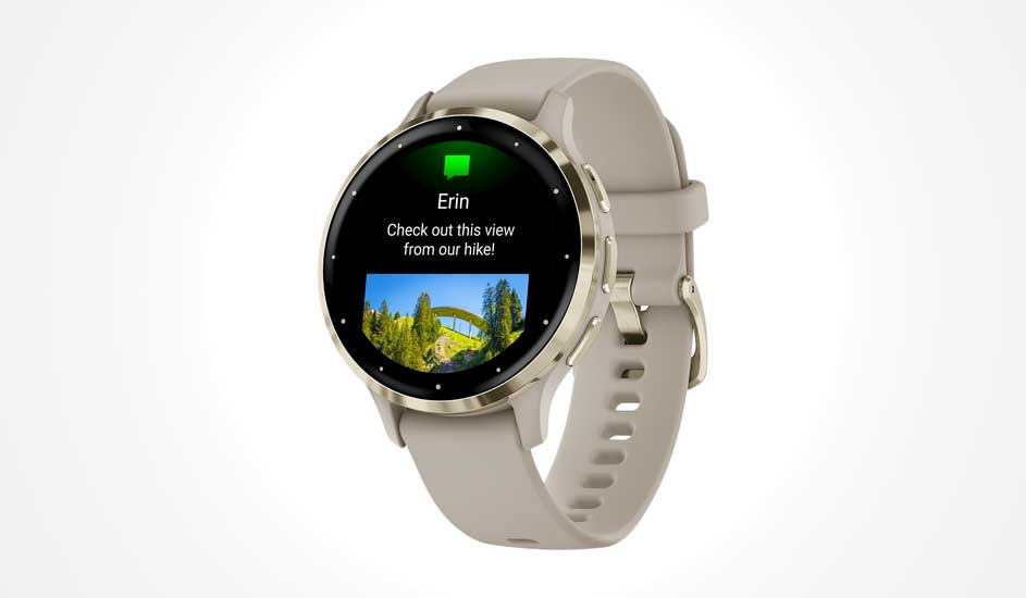 Une montre connectée beige affiche un message avec texte, nom et photo d’un pont dans un paysage vert sur son écran rond.