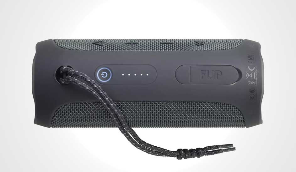 Grijze JBL Flip luidspreker met aan/uit-knop, batterij-indicator, en een koord, liggend op een witte ondergrond.