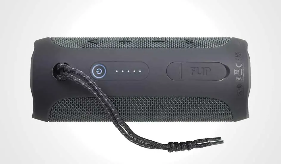 Grijze JBL Flip luidspreker met aan/uit-knop, batterij-indicator, en een koord, liggend op een witte ondergrond.