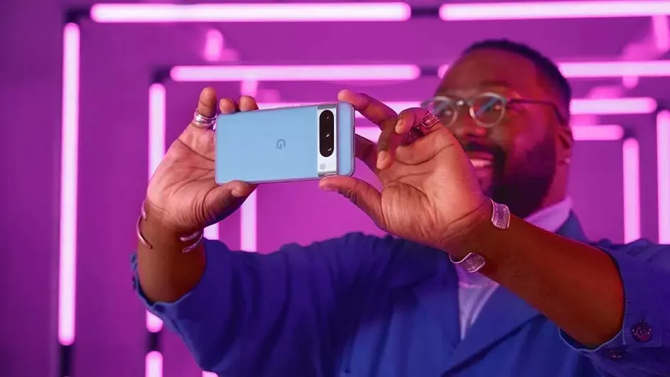 Een blauwe smartphone wordt vastgehouden tegen een achtergrond van roze neonlichten. De telefoon heeft een camera aan de achterkant.