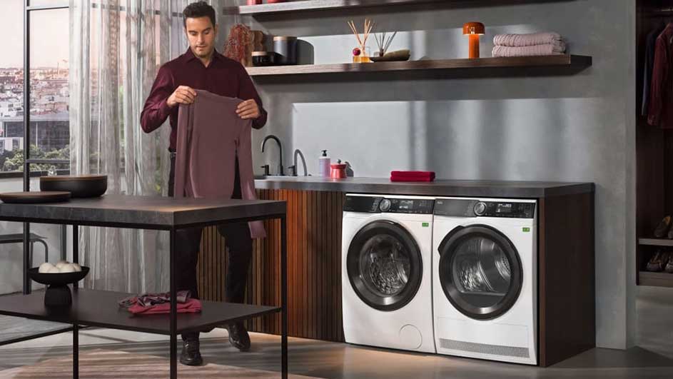 Witte wasmachines naast een donkere houten kast en een donkere tafel in een ruimte met rekken en een raam.