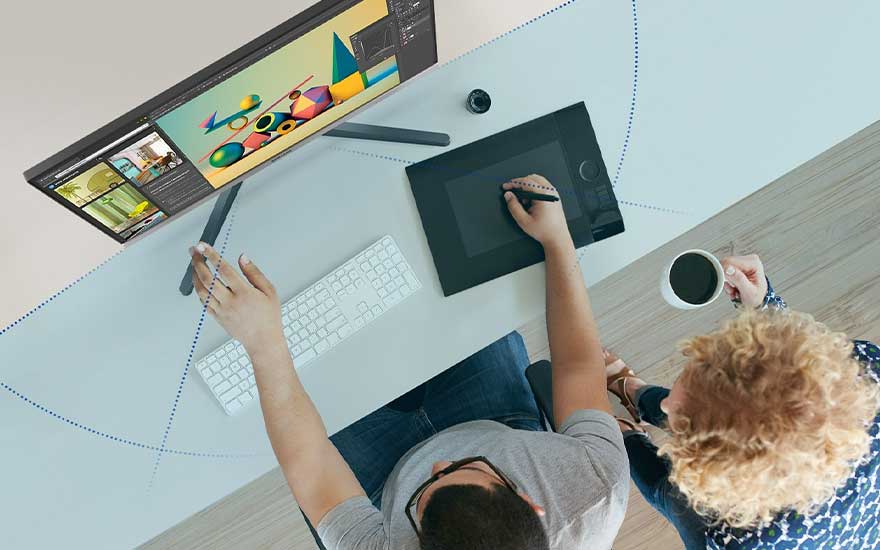 Vue du dessus d'un bureau avec un écran, une tablette graphique, un clavier et une tasse de café.
