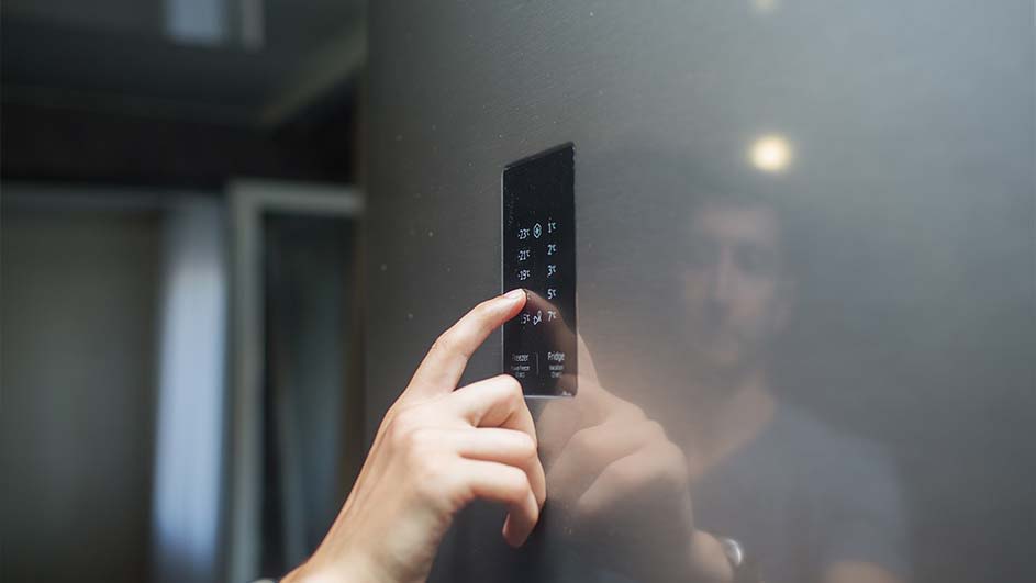 Une main appuie sur l'écran tactile d'un réfrigérateur gris. L'écran affiche des options de température.