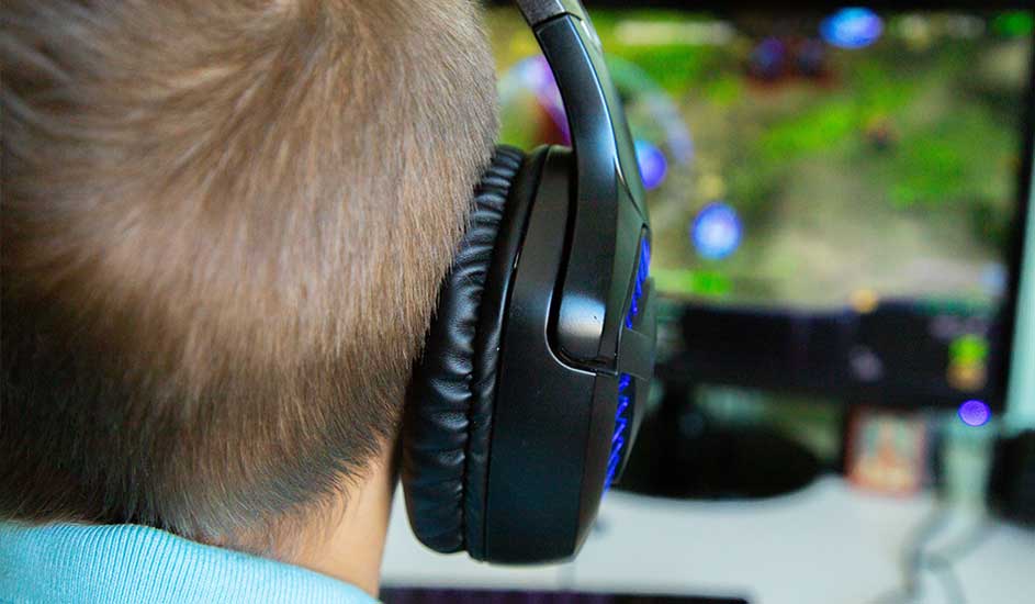 Zicht op de achterkant van een hoofd met een zwarte hoofdtelefoon met blauwe accenten, kijkend naar een monitor.