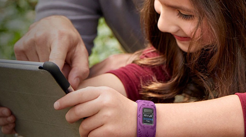 Une fille avec un bracelet violet utilise une tablette avec un adulte dans un cadre extérieur verdoyant.