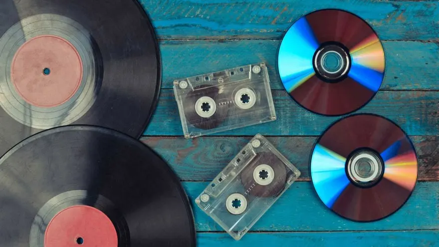 Disques vinyles, cassettes audio et CD sur une table bleue.