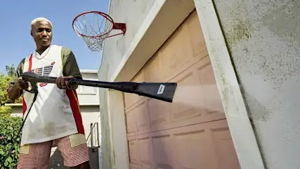Une personne nettoie les dalles de béton de la terrasse avec un nettoyeur haute pression en portant des bottes en caoutchouc devant une maison contemporaine.