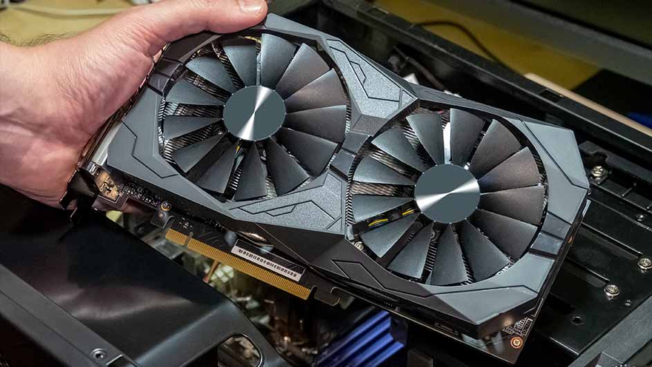 Une main tient une carte graphique grise à double ventilateur au-dessus d'un ordinateur.