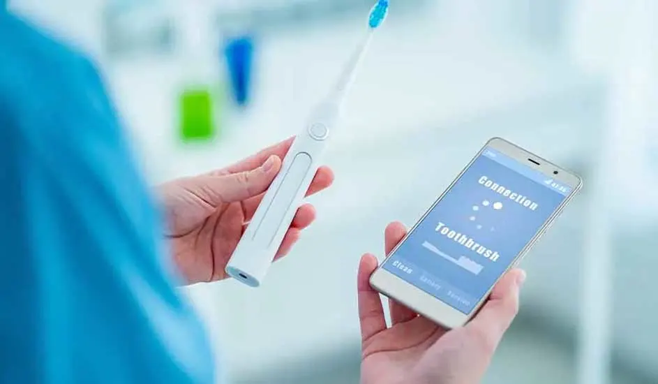 Een persoon houdt een witte elektrische tandenborstel en een smartphone vast met een blauw scherm.
