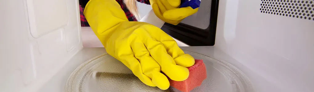 Een gele handschoen houdt een rode spons vast in een witte magnetron.