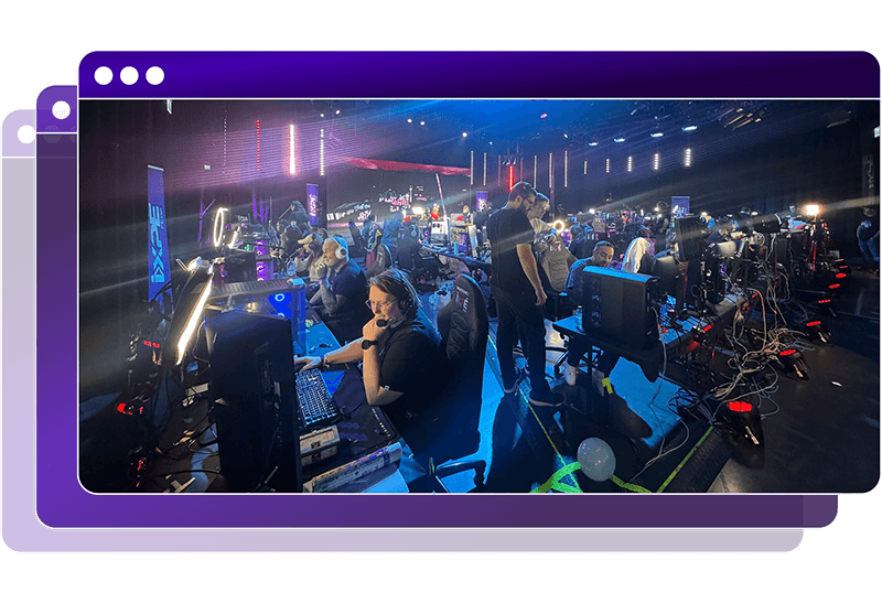 Groot stream event in een donker verlichte zaal; tientallen mensen gamen aan pc’s met headsets, kabels en studioverlichting rondom.