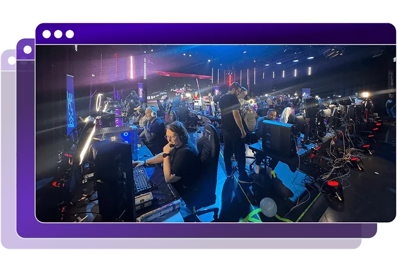 Groot stream event in een donker verlichte zaal; tientallen mensen gamen aan pc’s met headsets, kabels en studioverlichting rondom.